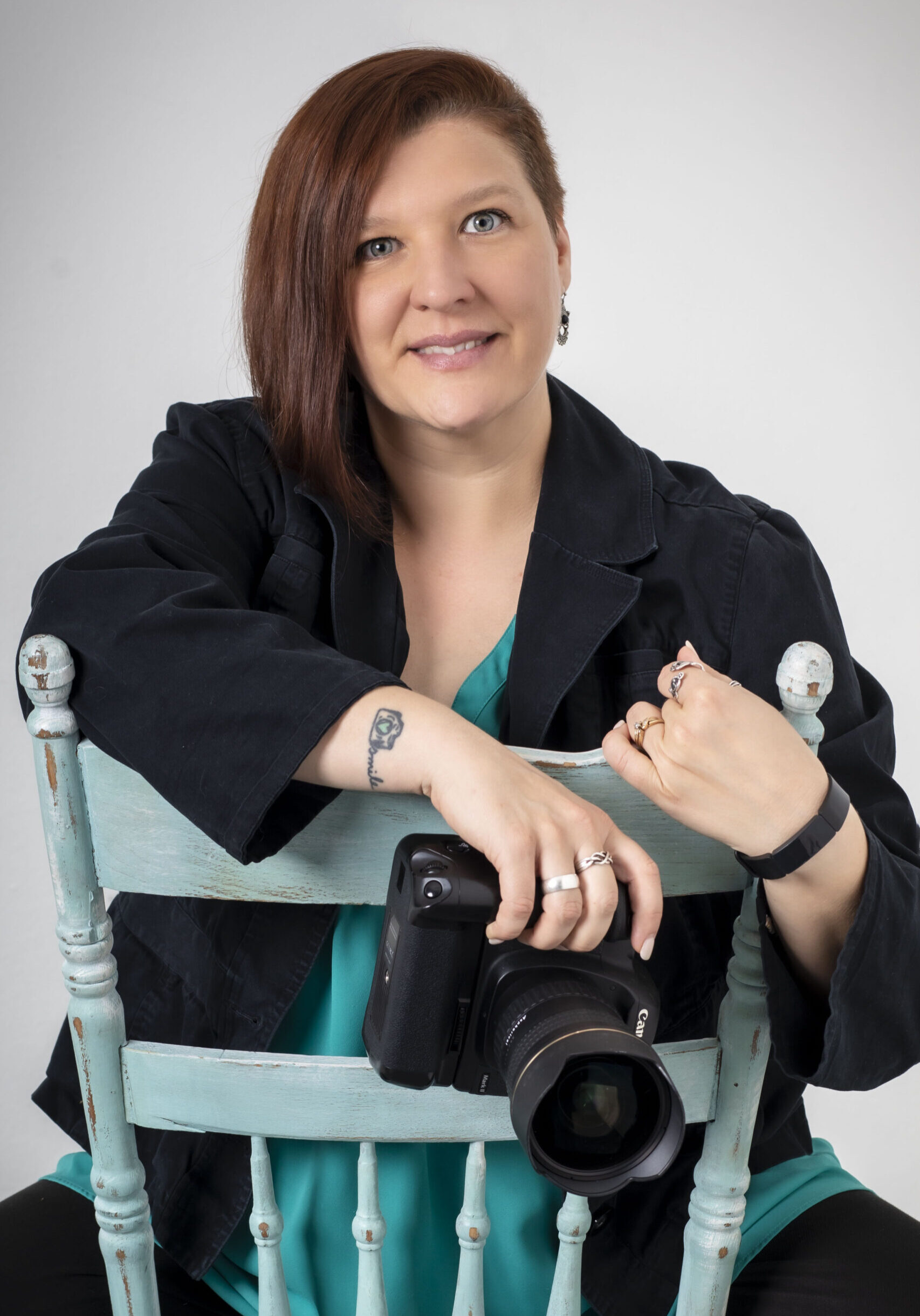 Person with short hair, wearing a black jacket, seated on a blue chair, holding a camera. - Duvall Chamber