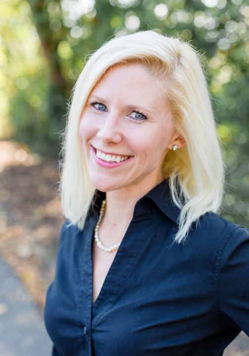 Woman with blonde hair wearing a black shirt, smiling outdoors with blurred greenery in the background. - Duvall Chamber